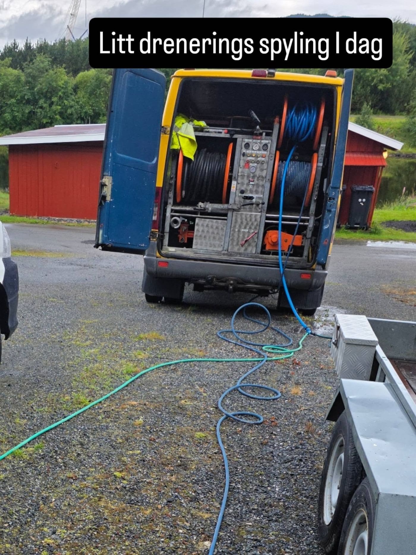 Spylebilen i arbeid på et gårdstun med slangen lagt ut og rød låve i bakgrunnen
